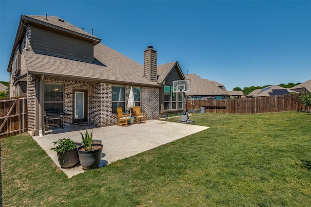 back of house with a chimney, a fenced backyard, a yard, brick siding, and roof with shingles