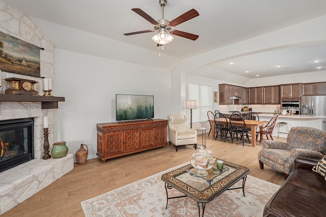 living room with light wood-type flooring, vaulted ceiling, recessed lighting, a ceiling fan, and a stone fireplace