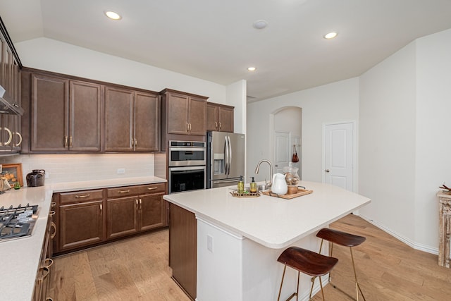 kitchen featuring stainless steel appliances, light countertops, arched walkways, light wood-style floors, and a breakfast bar