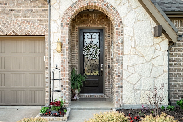 doorway to property with brick siding, an attached garage, roof with shingles, and stone siding