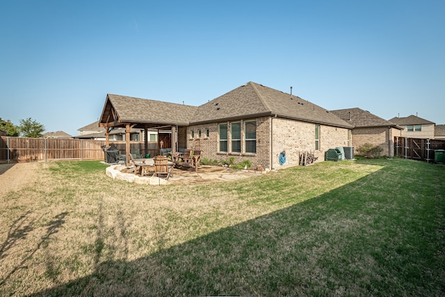 rear view of house featuring a shingled roof, a fenced backyard, a yard, a patio, and brick siding