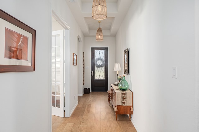 doorway featuring a chandelier, light wood-style floors, baseboards, and a raised ceiling