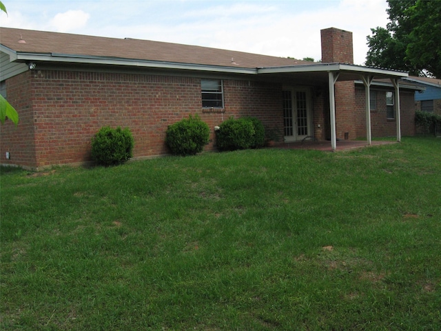 rear view of property with a chimney, a yard, a patio area, french doors, and brick siding