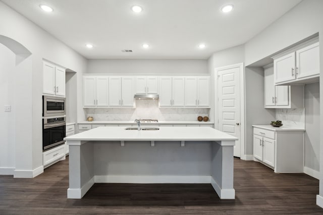 kitchen featuring light countertops, appliances with stainless steel finishes, a kitchen island with sink, and tasteful backsplash