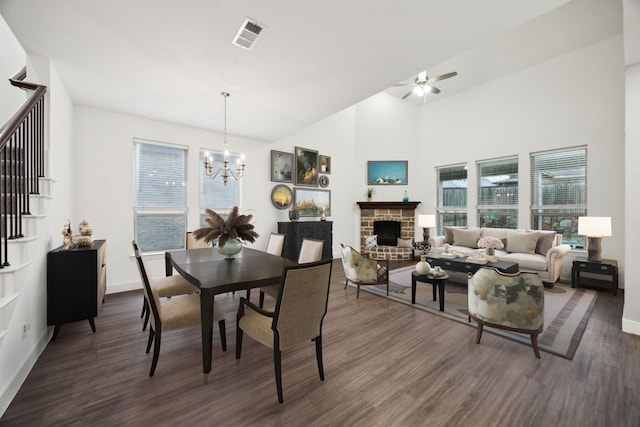 dining space with a stone fireplace, visible vents, dark wood finished floors, baseboards, and ceiling fan with notable chandelier
