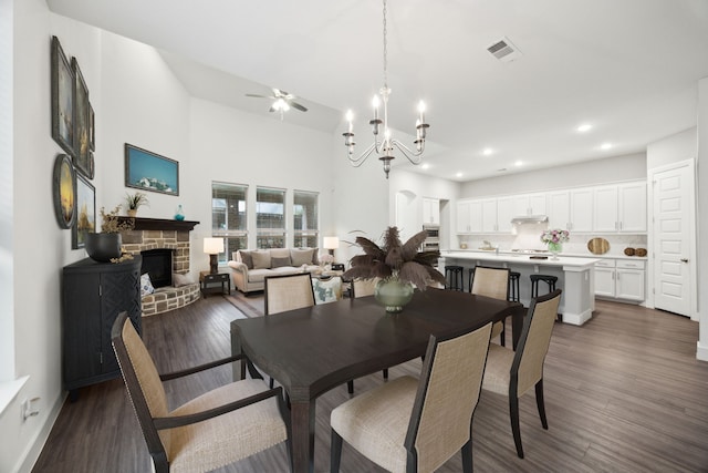 dining area featuring dark wood-style flooring, a stone fireplace, ceiling fan with notable chandelier, recessed lighting, and baseboards