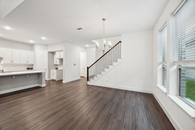 unfurnished living room featuring an inviting chandelier, baseboards, dark wood finished floors, and visible vents