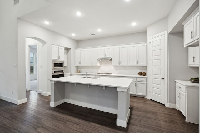 kitchen featuring appliances with stainless steel finishes, arched walkways, a sink, light countertops, and dark wood-style floors
