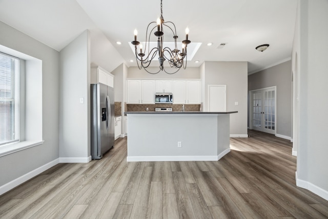 kitchen with white cabinets, stainless steel appliances, dark countertops, decorative backsplash, and a notable chandelier