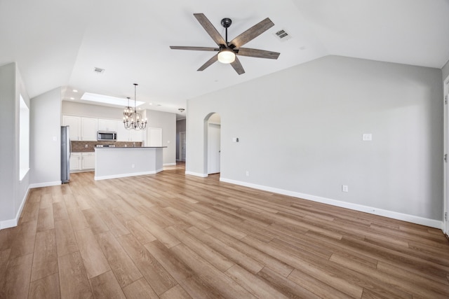 unfurnished living room with lofted ceiling, light wood-style flooring, baseboards, and ceiling fan with notable chandelier
