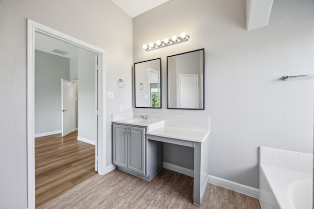 bathroom with wood finished floors, vanity, a tub to relax in, baseboards, and visible vents