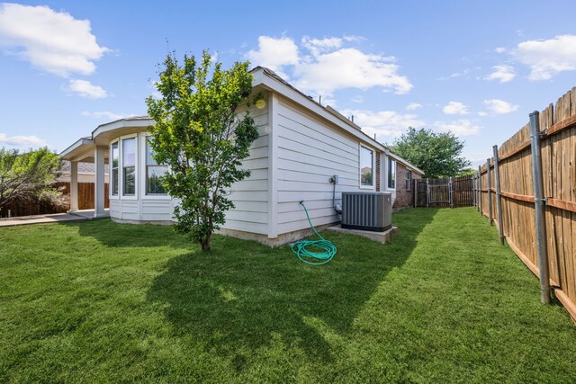 rear view of property with a fenced backyard, a yard, and central AC