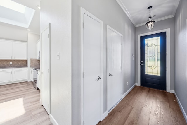 foyer entrance with light wood finished floors, baseboards, a notable chandelier, a skylight, and crown molding