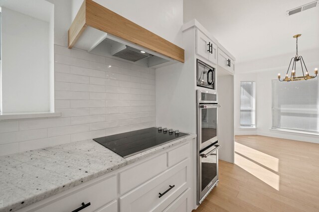 kitchen with backsplash, visible vents, premium range hood, black appliances, and an inviting chandelier