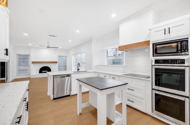 kitchen with a sink, light wood finished floors, appliances with stainless steel finishes, and a peninsula