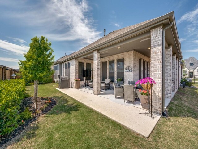 back of property featuring fence, a yard, a patio area, and brick siding