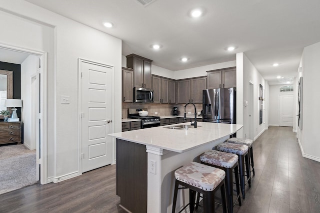 kitchen featuring stainless steel appliances, a sink, dark wood-style flooring, dark brown cabinetry, and a breakfast bar