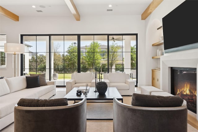 living room with beamed ceiling, a glass covered fireplace, ceiling fan, and visible vents