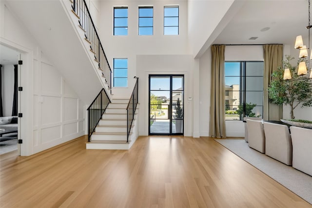 entryway with stairway, a decorative wall, light wood finished floors, and a towering ceiling