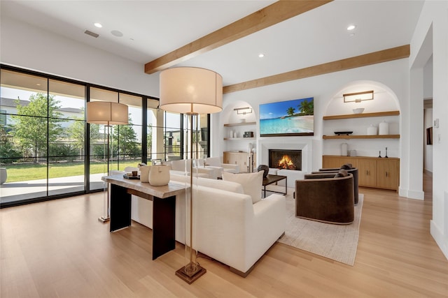 living room with visible vents, light wood-type flooring, beam ceiling, a lit fireplace, and built in shelves