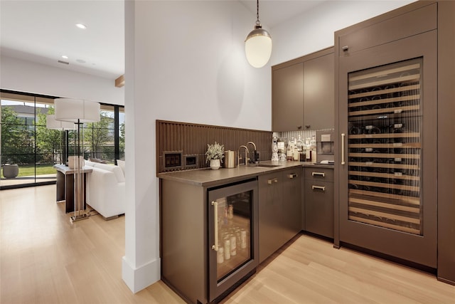 bar with indoor wet bar, beverage cooler, a sink, and light wood-type flooring