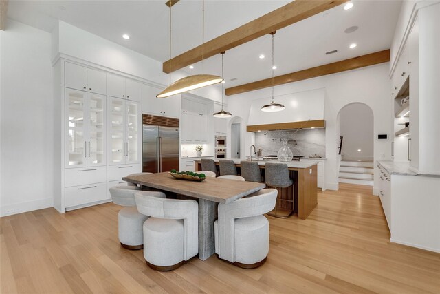 dining room featuring recessed lighting, beam ceiling, arched walkways, and light wood-style floors