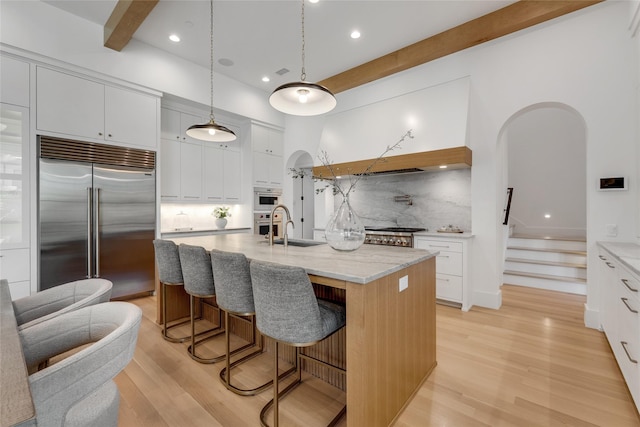 kitchen with light wood finished floors, a sink, beam ceiling, backsplash, and built in fridge