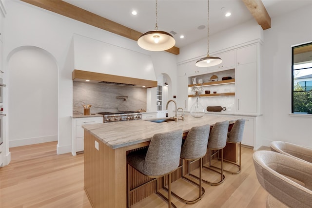 kitchen with arched walkways, a sink, light wood-style floors, beamed ceiling, and open shelves