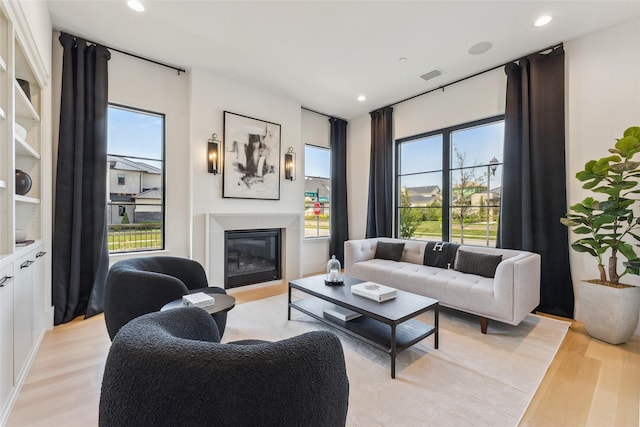 living room featuring recessed lighting, light wood-style floors, visible vents, and a glass covered fireplace