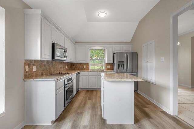 kitchen with white cabinets, a sink, decorative backsplash, a kitchen island, and appliances with stainless steel finishes