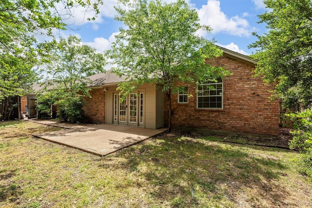 back of house featuring brick siding, french doors, a patio area, and a lawn