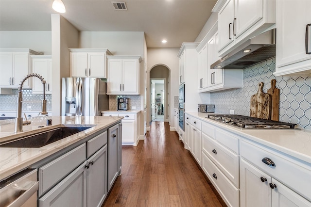560 Southwestern Dr, Rockwall, TX 75087 - kitchen featuring under cabinet range hood, a sink, stainless steel appliances, tasteful backsplash, and arched walkways