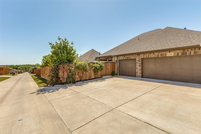 560 Southwestern Dr, Rockwall, TX 75087 - view of side of home with fence, driveway, a shingled roof, brick siding, and an attached garage