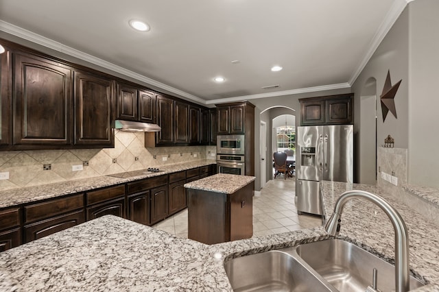 kitchen featuring under cabinet range hood, a sink, arched walkways, crown molding, and appliances with stainless steel finishes