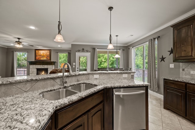 kitchen with stainless steel dishwasher, a sink, dark brown cabinetry, crown molding, and a stone fireplace