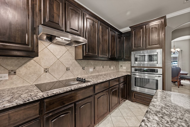 kitchen featuring arched walkways, under cabinet range hood, light stone countertops, and stainless steel appliances