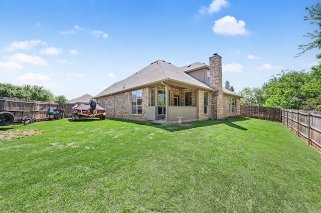 back of house featuring a chimney, a shingled roof, a fenced backyard, a lawn, and brick siding