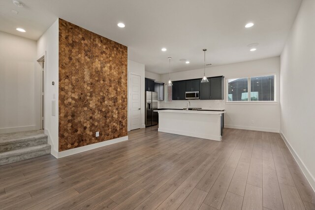 kitchen featuring stainless steel appliances, light countertops, dark cabinetry, baseboards, and a kitchen island with sink