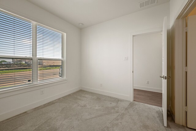 empty room with baseboards, visible vents, a wealth of natural light, and light colored carpet