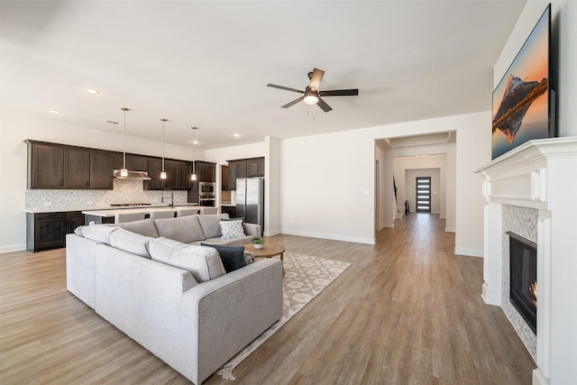 living area featuring a ceiling fan, baseboards, a glass covered fireplace, and light wood-type flooring