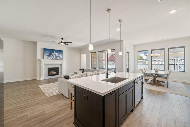 kitchen featuring baseboards, a warm lit fireplace, light wood-type flooring, a sink, and dishwasher