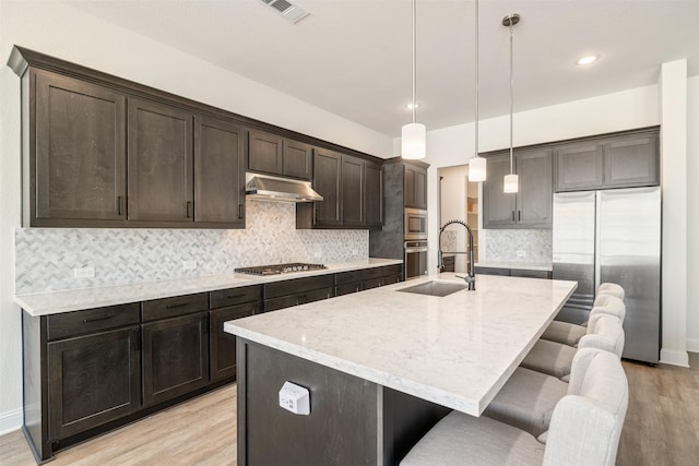 kitchen featuring visible vents, light wood-type flooring, under cabinet range hood, a sink, and stainless steel appliances