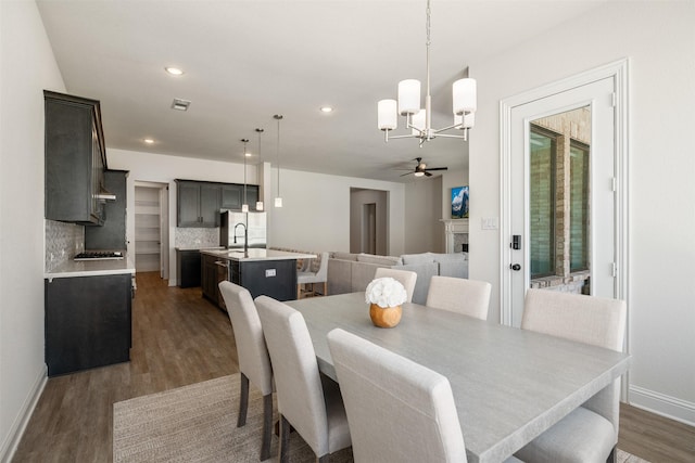 dining room with a fireplace, dark wood finished floors, ceiling fan with notable chandelier, baseboards, and visible vents