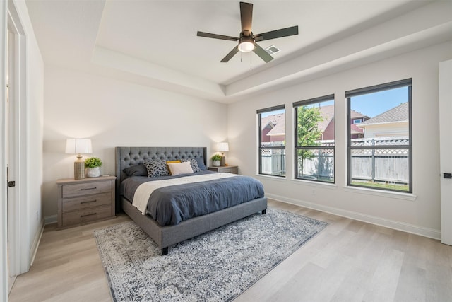 bedroom featuring a ceiling fan, visible vents, light wood-type flooring, a raised ceiling, and baseboards