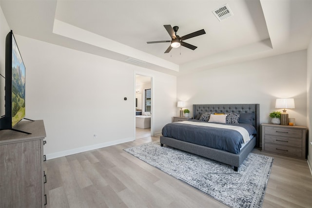bedroom with baseboards, visible vents, a raised ceiling, and light wood-style floors
