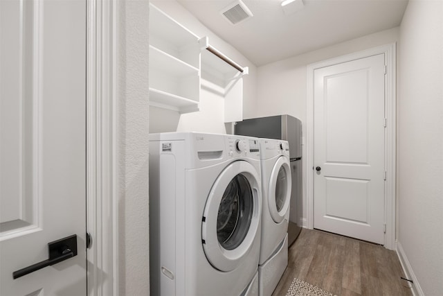 clothes washing area featuring laundry area, baseboards, wood finished floors, visible vents, and washing machine and dryer