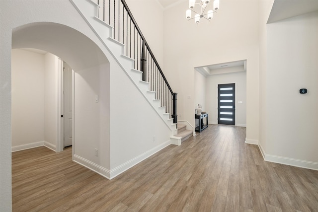foyer with arched walkways, a notable chandelier, stairway, and light wood-style floors