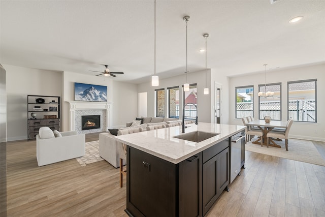 kitchen with light wood-style floors, stainless steel dishwasher, a sink, baseboards, and a glass covered fireplace