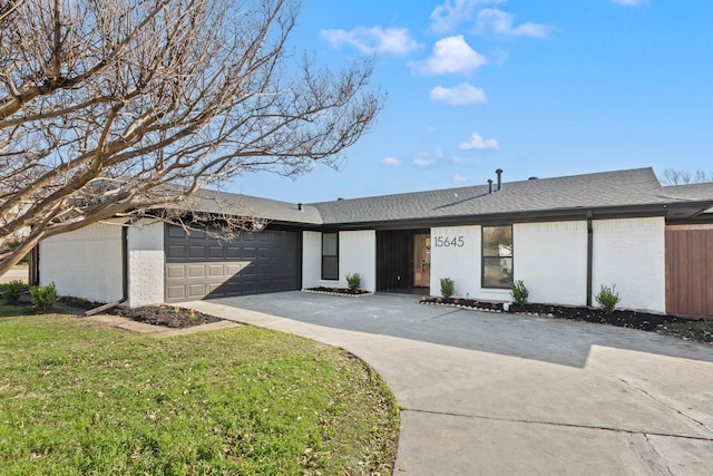 ranch-style house with concrete driveway, a front lawn, an attached garage, brick siding, and roof with shingles