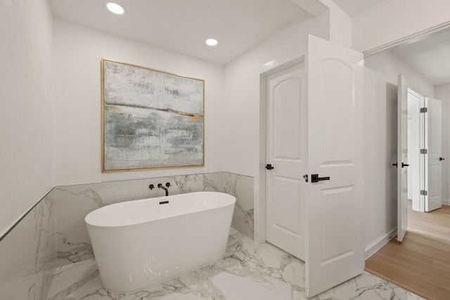 full bathroom with recessed lighting, marble finish floor, a wainscoted wall, tile walls, and a soaking tub